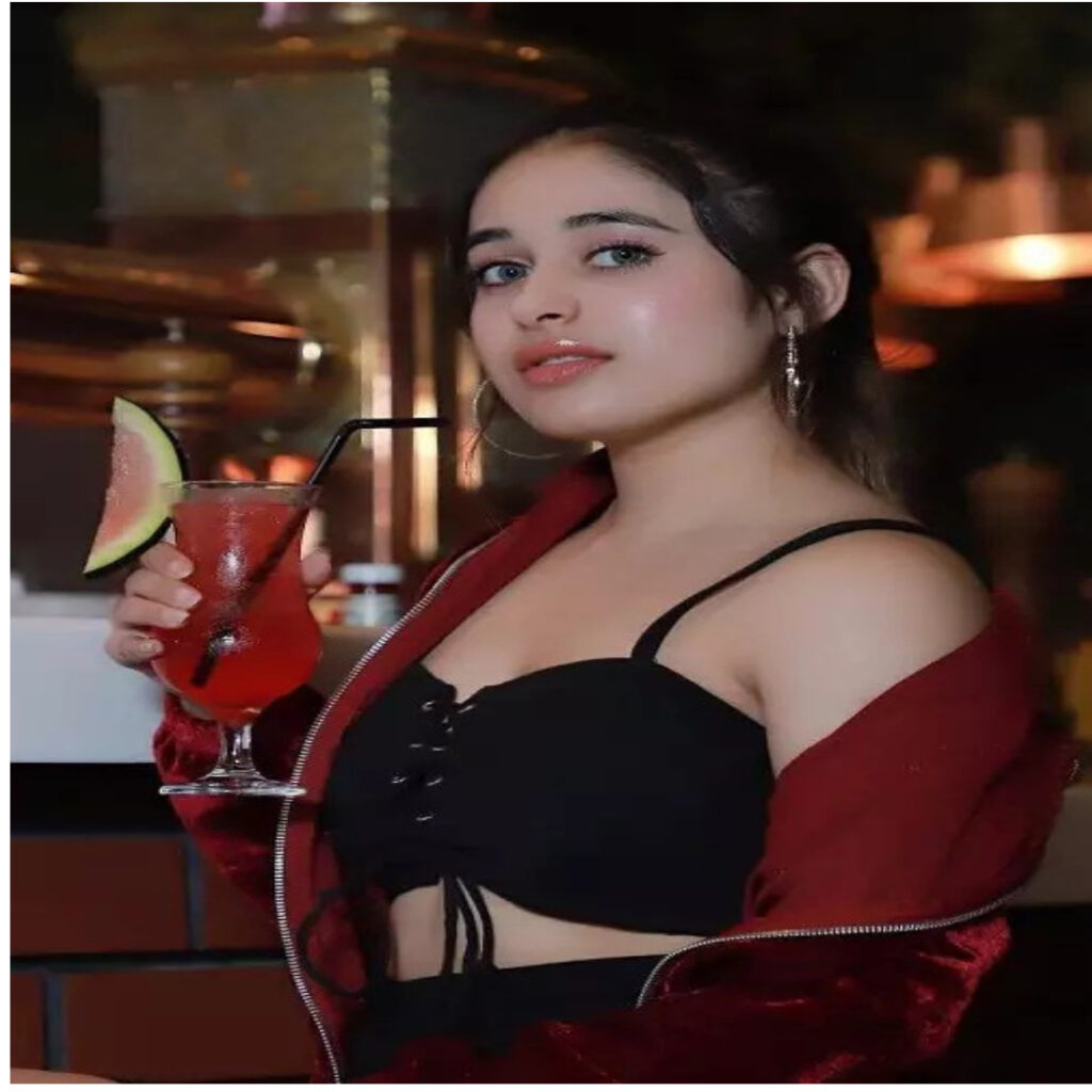 A GIRL SEXY LOOKS 24 YEARS OLD NAME IS MAMTA WEARING MAROON JACKET AND BLACK DRESS TAKING JUSE ON HER HAND IN STANDING POSITION
